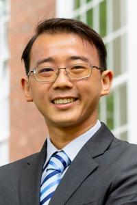 A smiling Asian man wearing a jacket and tie